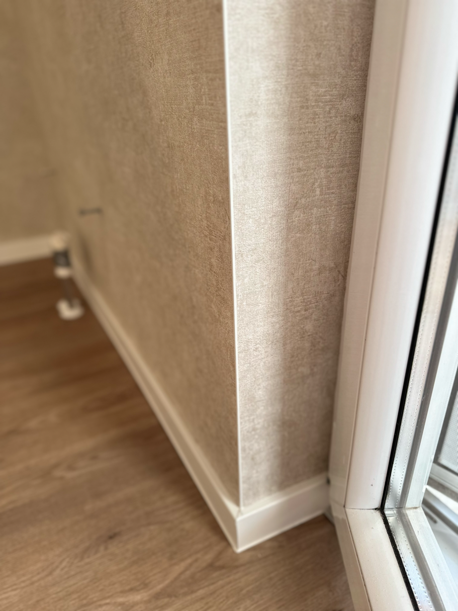 Eckbereich mit heller Wand, Fußleiste und Holzfußboden.