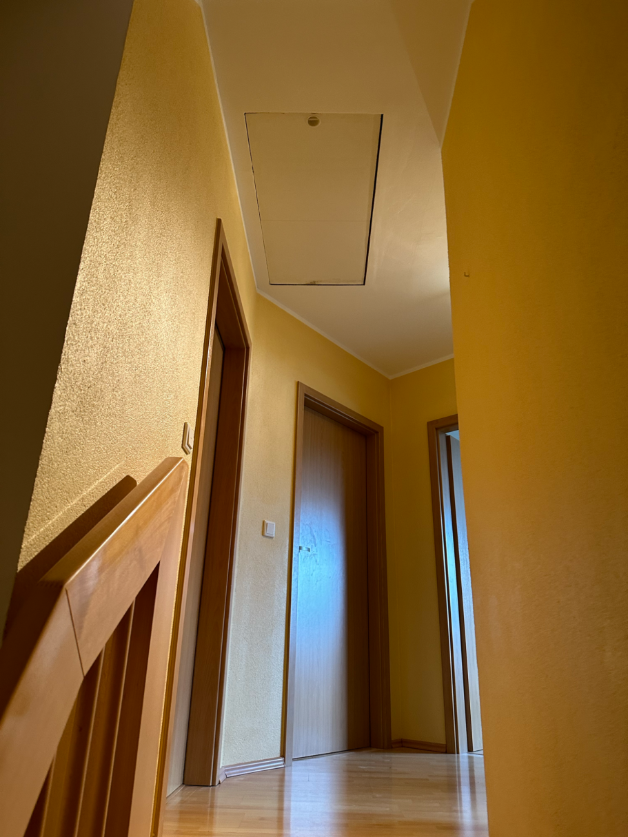 Ein langer Flur mit gelben Wänden und geschlossenen Türen auf beiden Seiten.